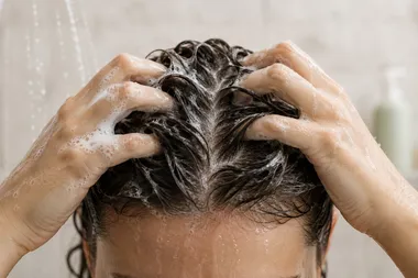 Person massaging medicated shampoo into wet hair in the shower